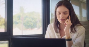 Ofiste çalışırken, beyaz bluzlu bir iş kadını telefonla konuşuyor. Ortalama çekim, yavaş çekim.