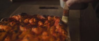 Şef taze pişmiş pizza hamuruna domates sosu ile zeytin yağı sürüyor. Yaklaşın, ağır çekim..