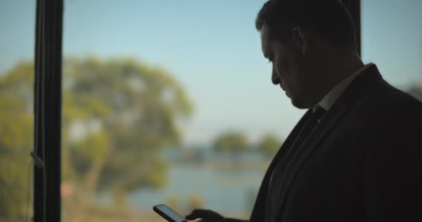 Бізнесмен Перевіряє Свій Телефон Стоячи Біля Вікна Дивлячись Назовні Повільний — стокове відео