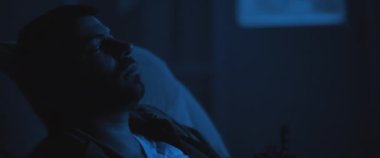 TSSB ile uğraşan, sandalyesinde oturan yetişkin bir asker. Orta boy, gerçek zamanlı, sinematik, mavi ışıklı.