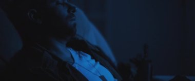 Yalnız ve bunalımlı asker elinde tüfekle koltukta oturuyor, travma sonrası stres bozukluğuyla uğraşıyor. Orta boy, gerçek zamanlı, sinematik, mavi ışıklı.