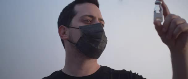 一个戴着黑色面具 穿着黑色衬衫 拿着一瓶疫苗的男人 — 图库视频影像