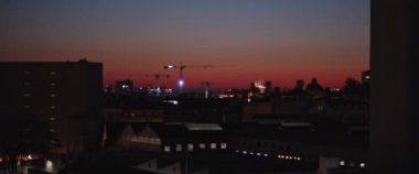 Gece şehrin üzerinde kırmızı gün batımı. Arka planda inşaat alanı var. Yavaş çekim.