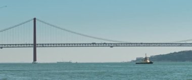 Lizbon 'da 25 Nisan süspansiyon köprüsünün altında hareket eden küçük bir gemi. Yavaş çekim.