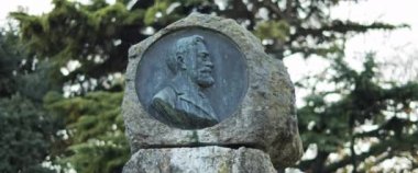 Şehir parkındaki yeşil arka plandaki taş anıt portresi. Yavaş çekim.