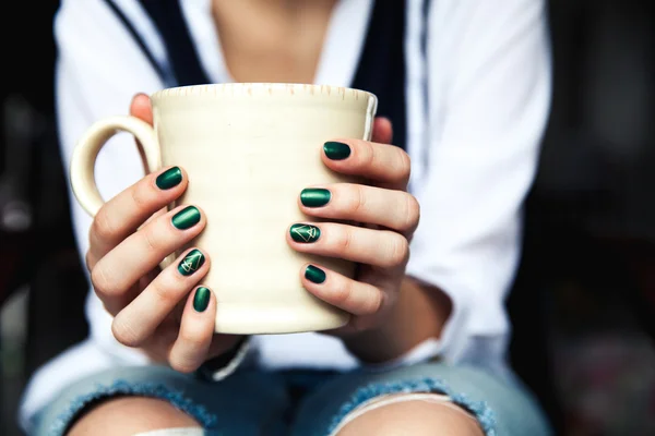Stilvolles modisches Mädchen mit einer Tasse Kaffee und einer grünen Maniküre in Jeans. Mode, Pflege, Schönheit — Stockfoto