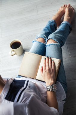 Genç modern kız büyük bir bardak ile kitap okuma yırtık kot pantolon