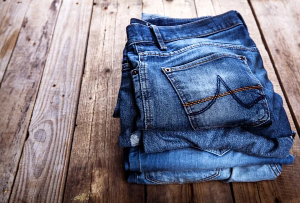 Jeans stacked on a wooden background — Stock Photo, Image