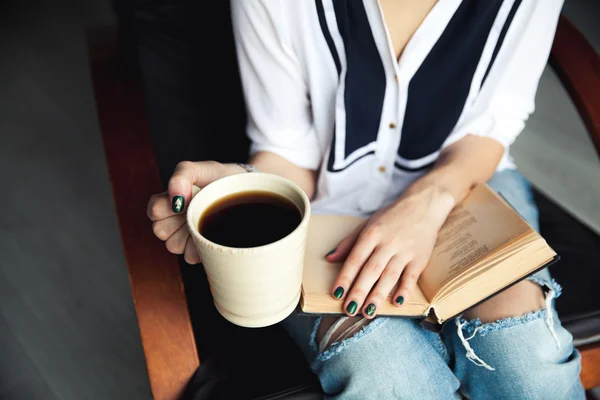 Mladá moderní dívka v roztrhané džíny čtení knihy s velkým šálkem kávy. Móda, životní styl, životní styl, rekreace, vzdělání, Koníčky. — Stock fotografie