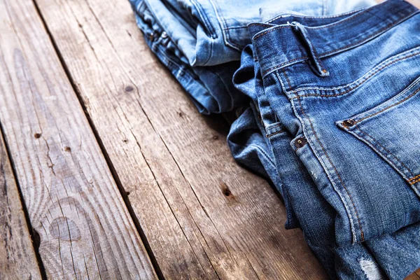 Jeans stacked on a wooden background — Stock Photo, Image