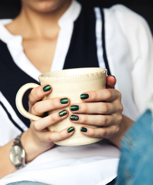 Snygg modern tjej med en kopp kaffe och en grön manikyr i jeans. Mode, vård, skönhet — Stockfoto