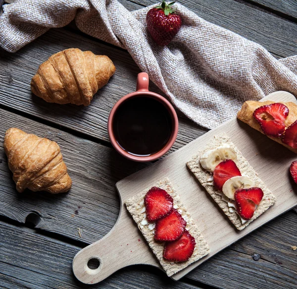 Läcker frukost med en kopp kaffe och frukt smörgåsar, croissanter. Jordgubbar, mat, dryck, choklad. — Stockfoto