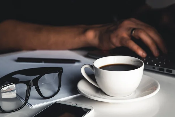 Человек печатает на ноутбуке, бизнес-концепцию, очки, чашку кофе и ручку на сером фоне. — стоковое фото