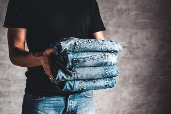 Close up stack of folded denim blue jeans in hand over gray wall background — Stock Photo, Image