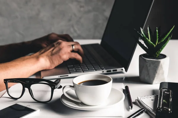 Un uomo digita su un computer portatile, concetto di business, occhiali, una tazza di caffè — Foto Stock