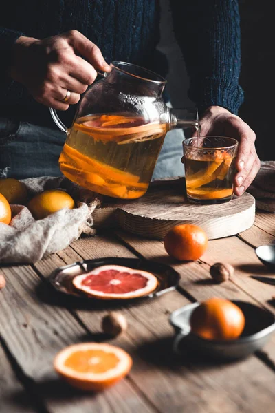 Mężczyzna nalewa herbatę cytrusową na drewniany stół. Zdrowy napój w stylu vintage. Wegańskie — Zdjęcie stockowe