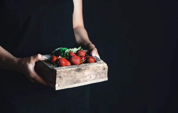 Dziewczyna w fartuchu trzyma drewniane pudełko z czerwonymi świeżymi truskawkami. Soczyste, letnie jagody. Witaminy, żywność ekologiczna. — Zdjęcie stockowe