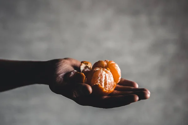 Coapte suculente mandarine portocalii dulci într-o mână umană pe un fundal întunecat . — Fotografie, imagine de stoc