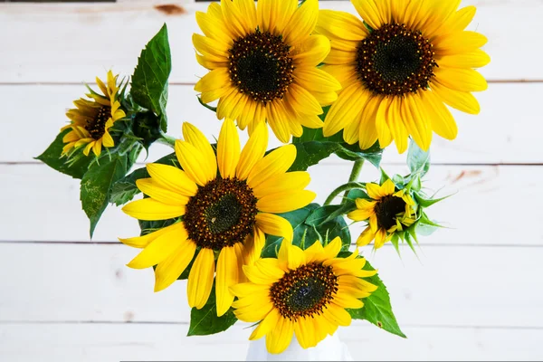 Un ramo de girasoles de otoño en un jarrón sobre una mesa de madera grumosa . — Foto de Stock