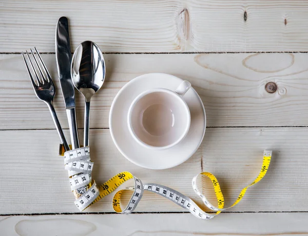 Assiette vide, tasse avec ruban à mesurer, couteau et fourchette. Alimentation diététique sur table en bois — Photo