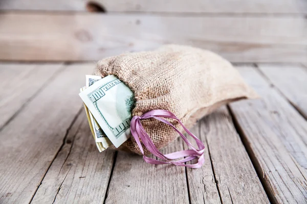 Dinero en bolsa de arpillera sobre fondo de madera —  Fotos de Stock