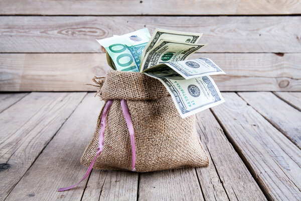 деньги в мешок из мешка на деревянном фоне
