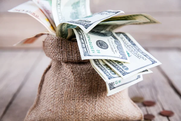 Dinheiro em pano de saco e moedas espalhadas em um fundo de madeira — Fotografia de Stock