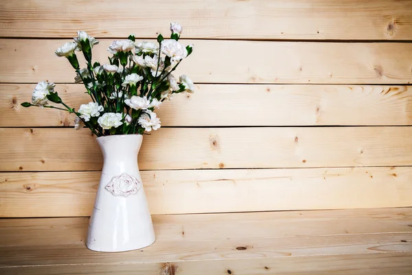 Delicate bouquet of carnations in a vase on a vintage wooden bac — Stock Photo, Image