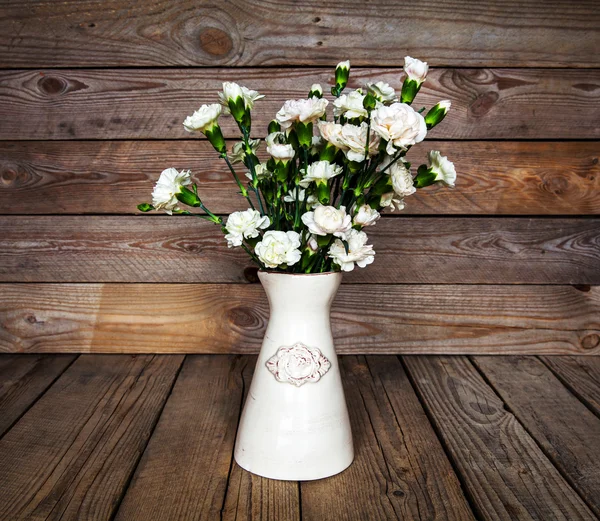 Delicate bouquet of carnations in a vase on a vintage wooden bac — Stock Photo, Image