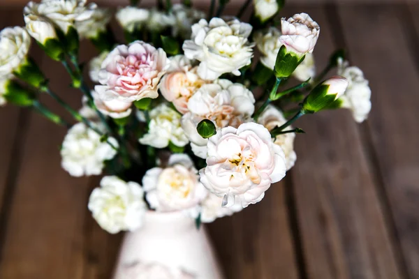 Delicate bouquet of carnations in a vase on a vintage wooden bac — Stock Photo, Image