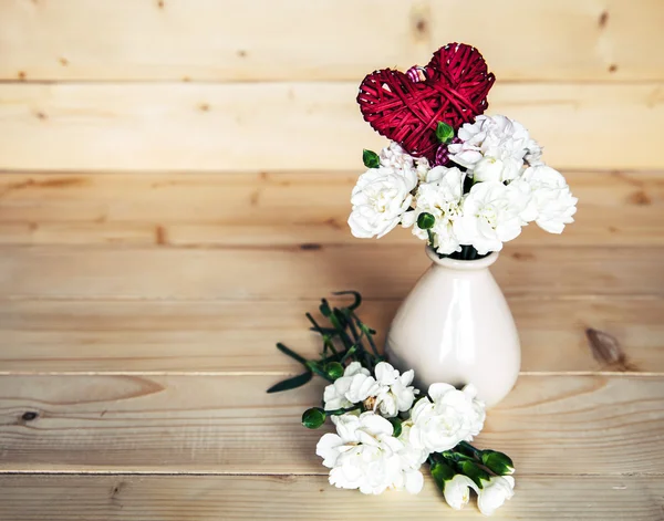 Delicate bouquet of carnations in vintage vase with heart on woo — Stock Photo, Image