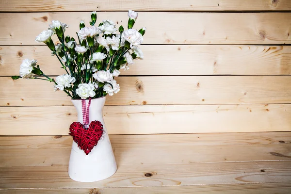 Delicate bouquet of carnations in vintage vase with heart on woo — Stock Photo, Image