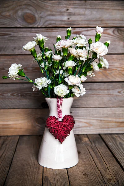 Delicate bouquet of carnations in vintage vase with heart on wooden background. Valentine's Day — Stock Photo, Image