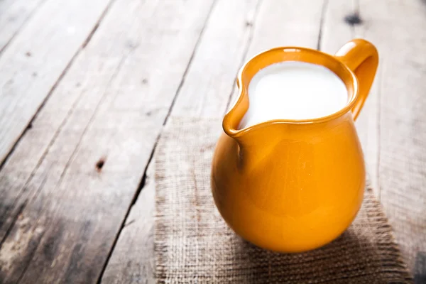 Clay milk jug isolated on wooden background — Stock Photo, Image