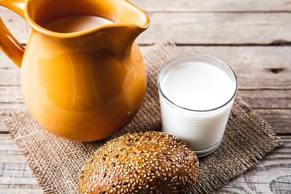 Milchkrug und eine Rolle auf dem hölzernen Hintergrund. Lebensmittel — Stockfoto