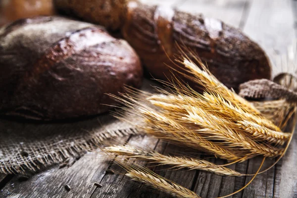 Сельский хлеб и пшеница на старинном деревянном столе. Темный капризный фон со свободным текстовым пространством . — стоковое фото