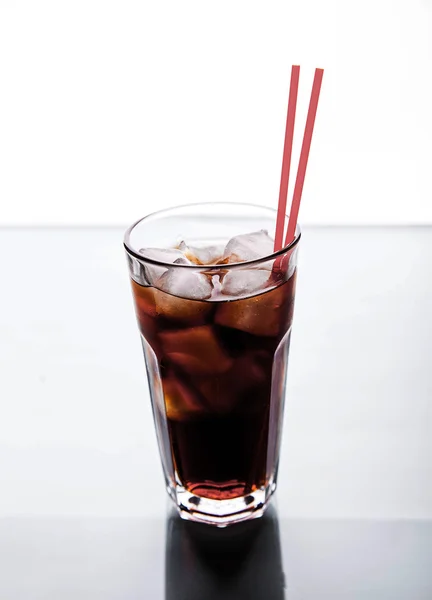Cola in un bicchiere con ghiaccio con tubo rosso. bevande analcoliche — Foto Stock