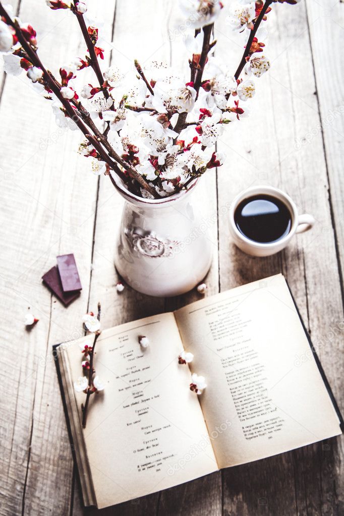 Open vintage book with blossom branch of cherry-tree on  wooden table with a beautiful vintage vase. a cup of coffee