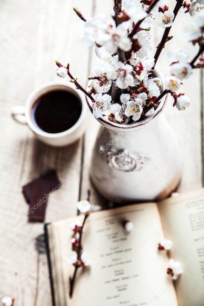 Open vintage book with blossom branch of cherry-tree on  wooden table with a beautiful vintage vase. a cup of coffee