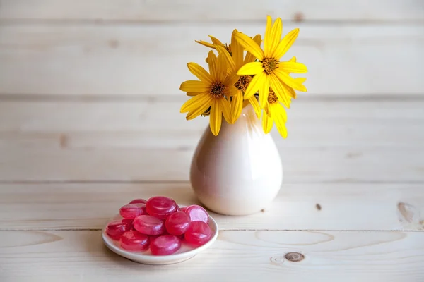 Flores amarillas en un jarrón vintage con caramelos rojos en una ba de madera — Foto de Stock