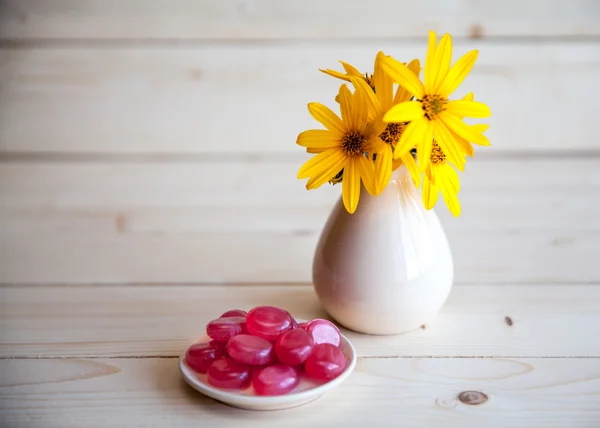 Flores amarelas em um vaso vintage com doces vermelhos em um fundo de madeira — Fotografia de Stock