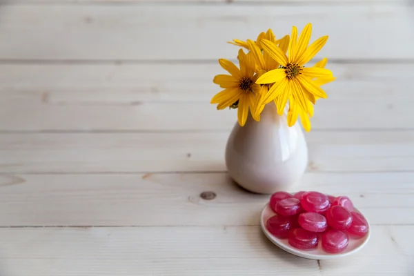 Flores amarelas em um vaso vintage com doces vermelhos em um fundo de madeira — Fotografia de Stock