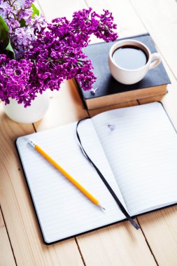 Beautiful lilac on office desk with a book and a cup of coffee and notebook