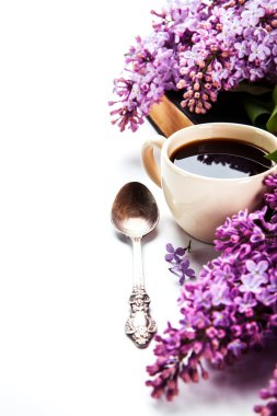 Black coffee in a cup, a spoon and fresh lilac flowers