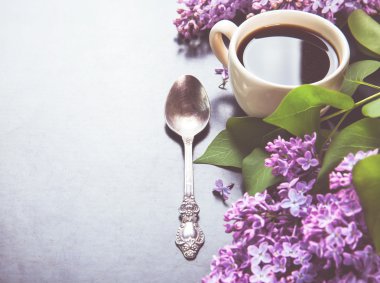 Black coffee in a cup, a spoon and fresh lilac flowers on black 