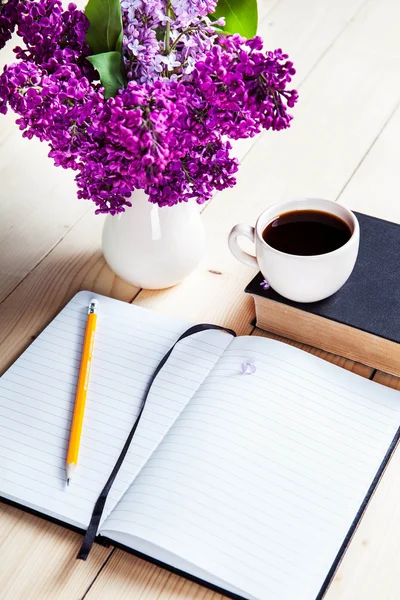 Beautiful lilac on office desk with a book and a cup of coffee and notebook — Stock Photo, Image