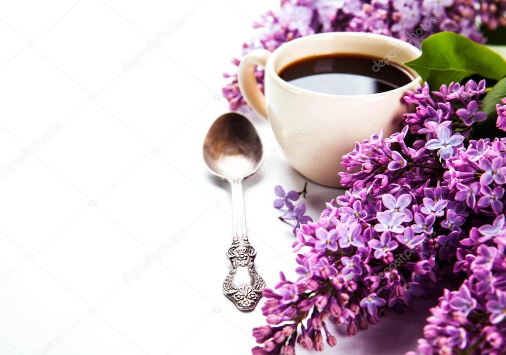 Black coffee in a cup, a spoon and fresh lilac flowers