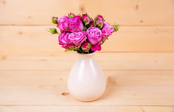 Roze rozen in een vaas op houten achtergrond — Stockfoto