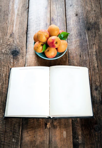 Deliciosa fruta. albaricoques con un libro sobre fondo de madera — Foto de Stock