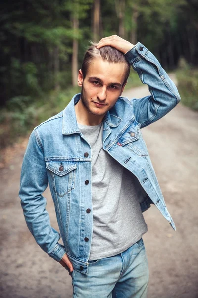 Joven hombre guapo en el bosque. jeans y chaqueta vaquera — Foto de Stock